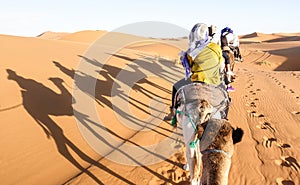 Tourists caravan riding dromedaries through sand dunes in Sahara desert near Merzuga in Morocco - Wanderlust travel concept