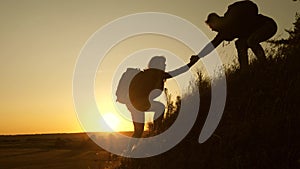 Tourists climb the mountain at sunset, holding hands. teamwork of business people. Traveler man holds out a woman`s hand
