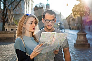 Tourists couple looking at the paper map and searching for direction early in the morning on empty ancient square