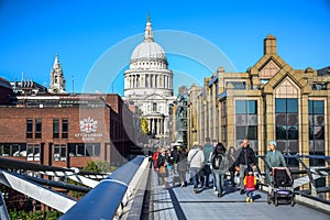 Tourists crossing the River Thames by walking through Millennium Bridge with Saint Paul`s Cathedral in background, London, UK