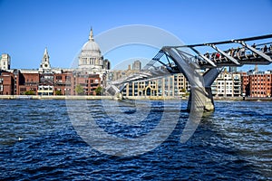 Tourists crossing the River Thames by walking through Millennium Bridge with Saint Paul`s Cathedral in background, London, UK