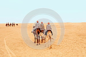 Tourists dressed in striped robes and orange turbans on their heads riding on two-humped camels for a walk