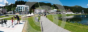 Tourists enjoy summer activities on the lakeshore in Arosa with the train and cable railway station in the background