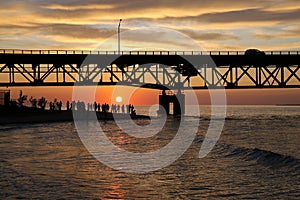 Tourists enjoying the view of sunset by Lake Michigan under Mackinac Bridge