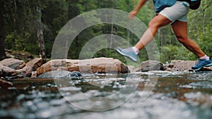 Tourists legs in hiking boots crosses stream flowing in forest, close up