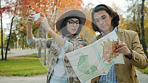 Tourists man and woman looking at map and taking pictures with smartphone outdoors