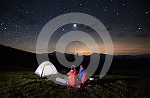 Tourists near campfire and tent under night starry sky