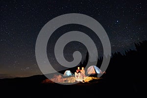 Tourists near campfire and tents under night starry sky