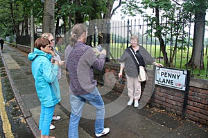 Tourists photograph each other in front of the street sign of Penny Lane. Liverpool, England.