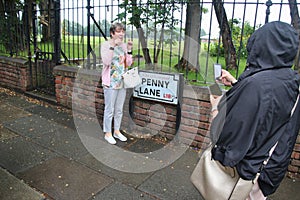 Tourists photograph each other in front of the street sign of Penny Lane. Liverpool, UK.