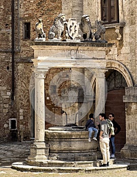 Tourists posing at The well of Griffins and Lions in the big square of Montepulciano, Italy.