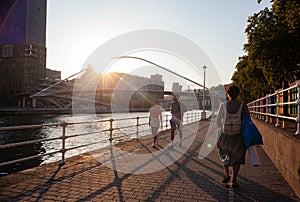 Tourists on the promenade next to the Nervion River near the Zubizuri Bridge at sunset, Bilbao Euskadi, Spain