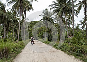 Tourists ridding a scooter on a country road, Thailand