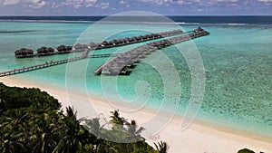 Tourists riding bicycles at overwater bungalows at tropical island luxury resort in Maldives. Sunny. Ocean. Sand. Aerial video.