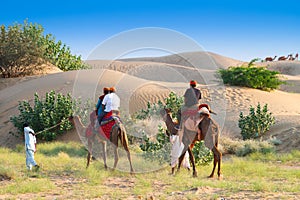 Tourists riding camels, Camelus dromedarius, at sand dunes of Thar desert. Camel riding is a favourite activity amongst all