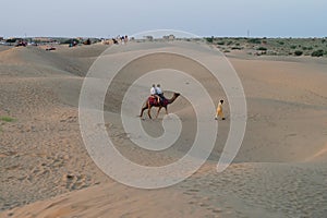 Tourists riding camels,  Camelus dromedarius, at sand dunes of Thar desert, Rajasthan, India. Camel riding is a favourite activity