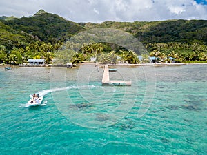 Tourists riding high speed jet boat in a stunning azure blue turquoise lagoon. Aerial view. Raiatea, French Polynesia.