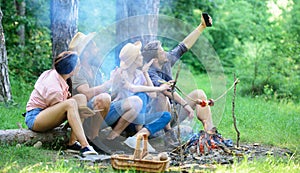 Tourists sit log near bonfire taking photo on smartphone. Friends on vacation capture moment. Man taking photo near