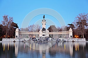 Tourists sit near monument to Alfonso XII at pond in Retiro Park