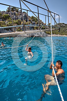 Tourists swimming in sea, holding on to rope walking yacht.