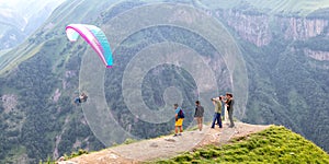 Tourists on top of a mountain pass, taking pictures of a flying paraglider