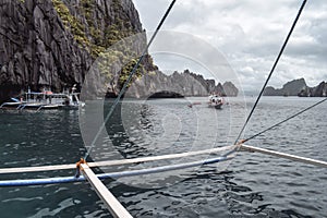 Tourists on traditional Philippino fisherman boats crossing the waters near grey limestone cliffs of El Nido at Palawan Island the