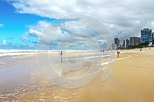 Tourists walk along wet beach by turbulent Pacific Ocean under stormy skies with tall towers of Surfers Paradise - Gold Coast Quee