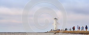 Tourists walk on the pier to a lighthouse on the Baltic Sea in Swinoujscie in Poland. With blurred cloudy sky in the background