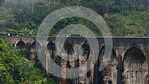 Tourists walk on stone bridge in jungle. Action. People walk on ancient stone bridge in rainforest. Beautiful landscape