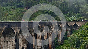 Tourists walk on stone bridge in jungle. Action. People walk on ancient stone bridge in rainforest. Beautiful landscape