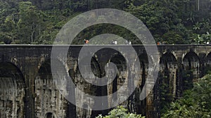 Tourists walk on stone bridge in jungle. Action. People walk on ancient stone bridge in rainforest. Beautiful landscape