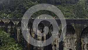 Tourists walk on stone bridge in jungle. Action. People walk on ancient stone bridge in rainforest. Beautiful landscape