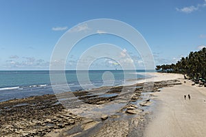 tourists walking along the beach with reefs between the beach and the sea at low tide