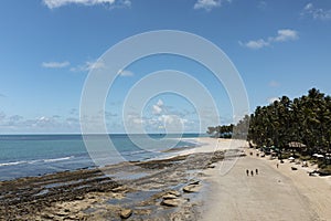 tourists walking along the beach with reefs between the beach and the sea at low tide