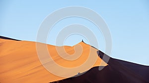 Tourists walking and sitting on the edge of a red sand dune at Sossusvlei National Park, a popular tourist destination in Namibia