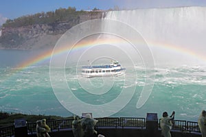 Tourists watch Niagara Falls tour boat under a full rainbow