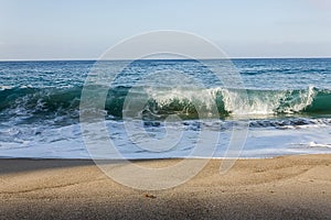 Tourqouise cresting transparent breaking in tube wave on sandy beach with backwash photo