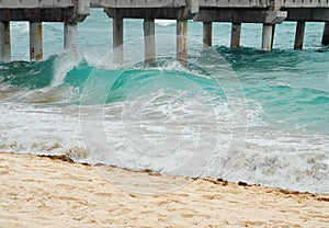 Tourquoise waves breaking on a beach next to a pier with sandy beach. photo