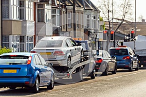 Tow truck delivers damaged vehicle staying on red traffic light in eglish city