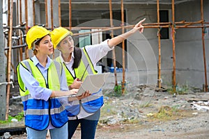 Tow young constructions woman in vest with yellow helmet working with laptop and holding radio while standing on building