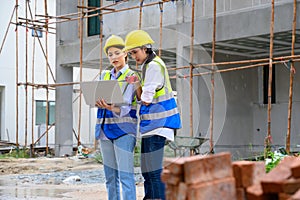 Tow young constructions woman in vest with yellow helmet working with laptop and holding radio while standing on building