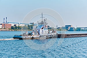 Towboat pushes dry bulk cargo barge on the river in an industrial landscape