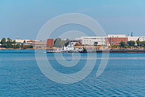 Towboat pushes dry bulk cargo barge on the river past the industrial landscape