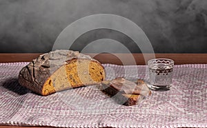 On a towel, bread, one piece  cut off with meay and a short glass of vodka on a black background