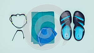 A towel with a cap, slates, swimming glasses and a smart bracelet on a blue background. Flat lay.
