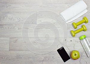 Towel, weights, water bottle, apple and phone on wooden background