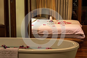 Towels, flowers and red rose petals decorations on the bed, flowers and petals in bathtub, concept of Honeymoon