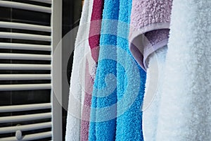 Towels hang next to a heated towel rail, wall radiator or radiator. White, blue, pink, red towels. Organization of