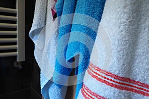 Towels hang next to a heated towel rail, wall radiator or radiator. White, blue, pink, red towels. Organization of