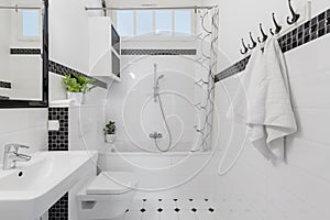 Towels and mirror in white and black bathroom interior with bath